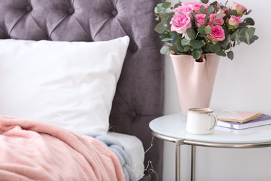 Photo of Cup of coffee and flowers on table near bed