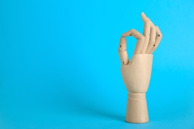 Wooden mannequin hand showing okay gesture on light blue background. Space for text