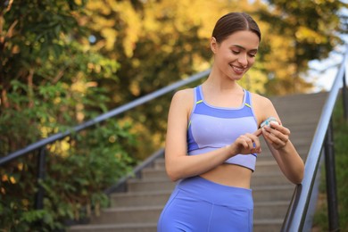 Photo of Attractive happy woman checking pulse with blood pressure monitor on finger after training in park. Space for text