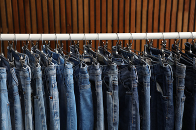 Rack with different jeans on wooden background