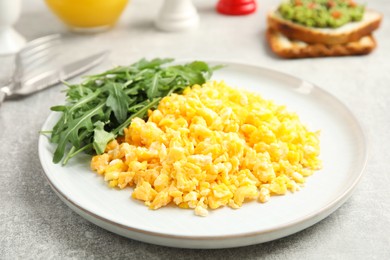 Tasty scrambled eggs with arugula served for breakfast on grey table