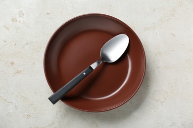 Empty brown ceramic plate with spoon on light grey table, top view