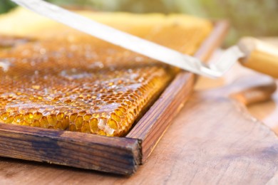Photo of Uncapping knife and honeycomb frame on wooden table outdoors, closeup