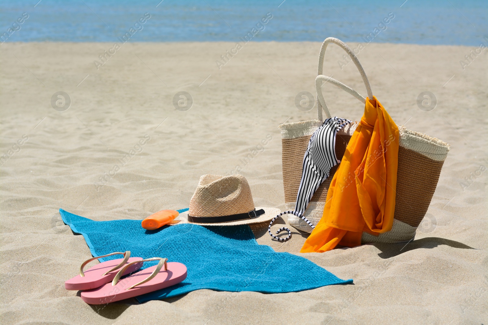 Photo of Blue towel, bag and beach accessories on sandy seashore