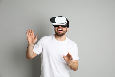 Photo of Happy man using virtual reality headset on light grey background