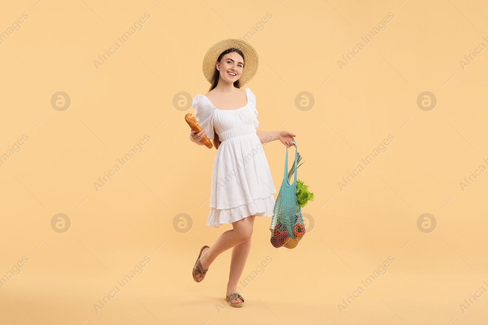 Photo of Woman with string bag of fresh vegetables and baguette on beige background