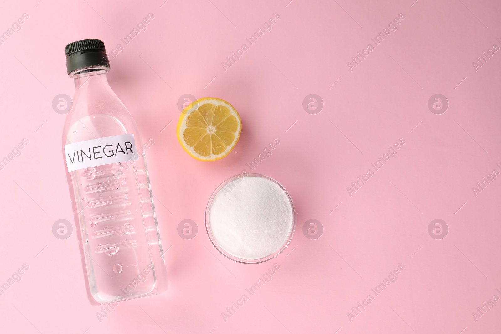 Photo of Eco friendly natural cleaners. Vinegar in bottle, cut lemon and bowl of soda on pink background, flat lay. Space for text