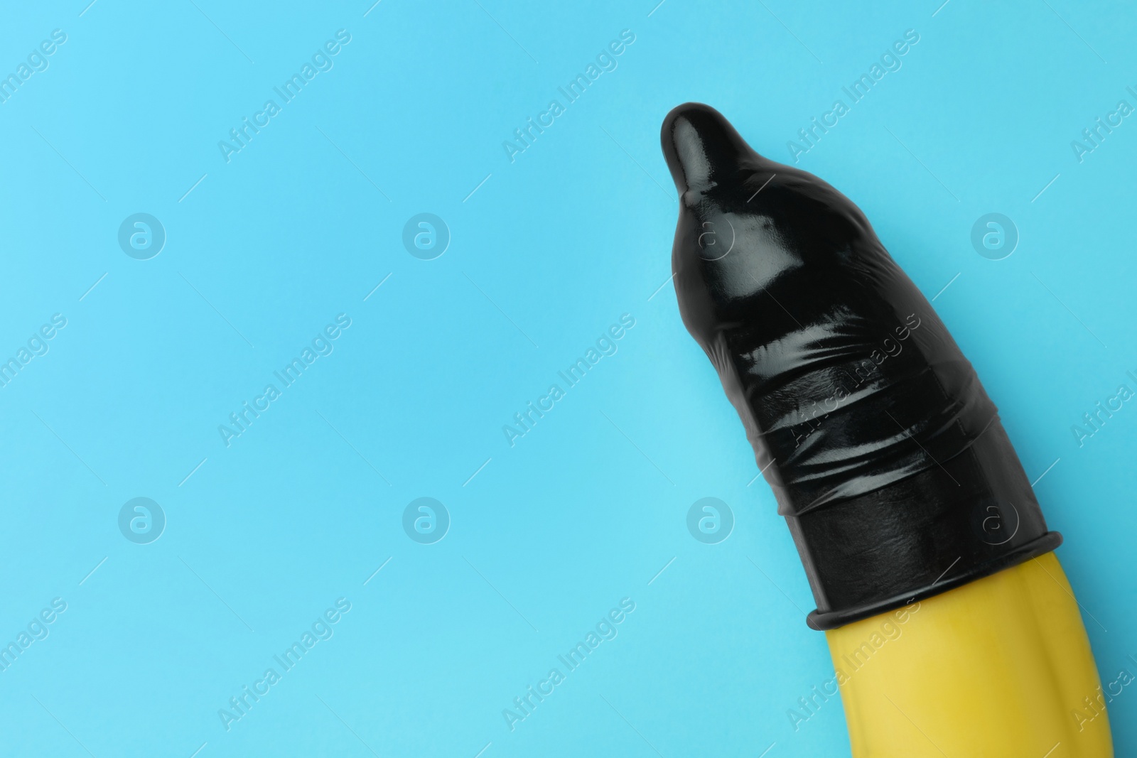 Photo of Banana with condom on light blue background, top view and space for text. Safe sex concept