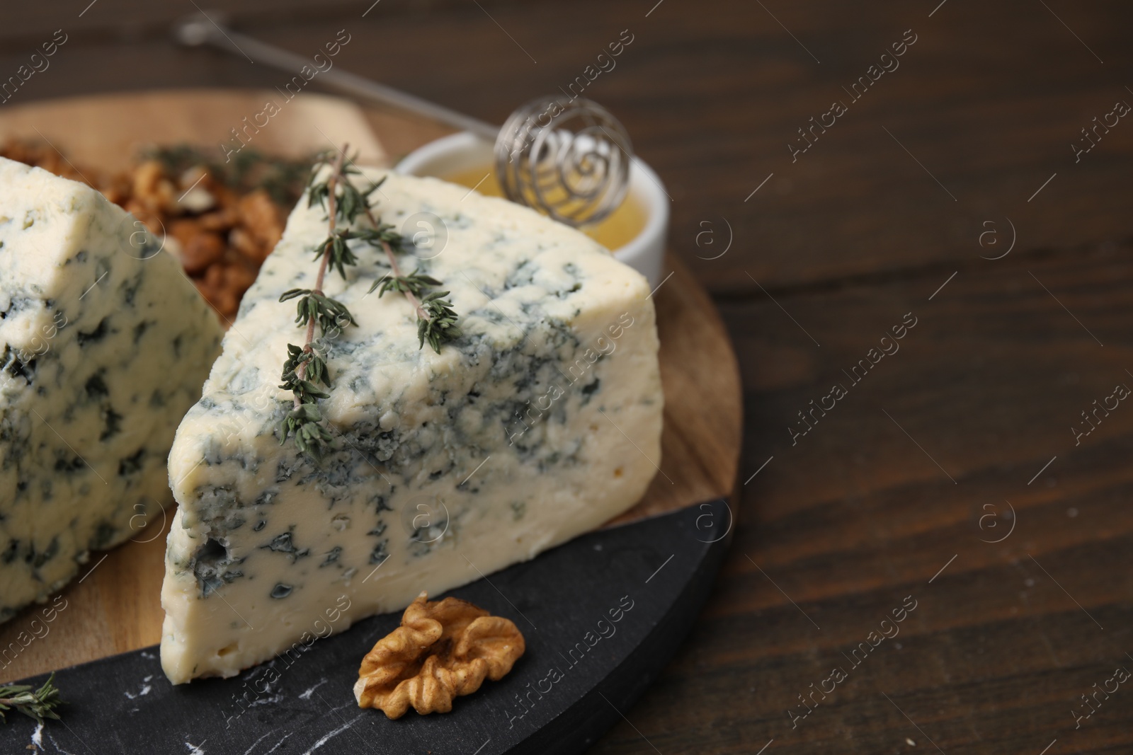Photo of Tasty blue cheese with thyme, honey and walnuts on wooden table, closeup. Space for text