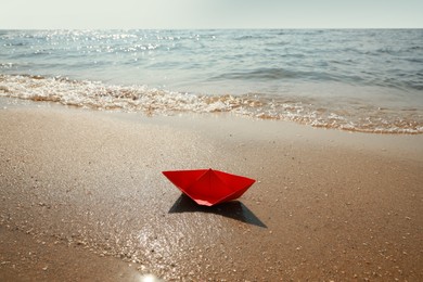 Red paper boat near river on sunny day