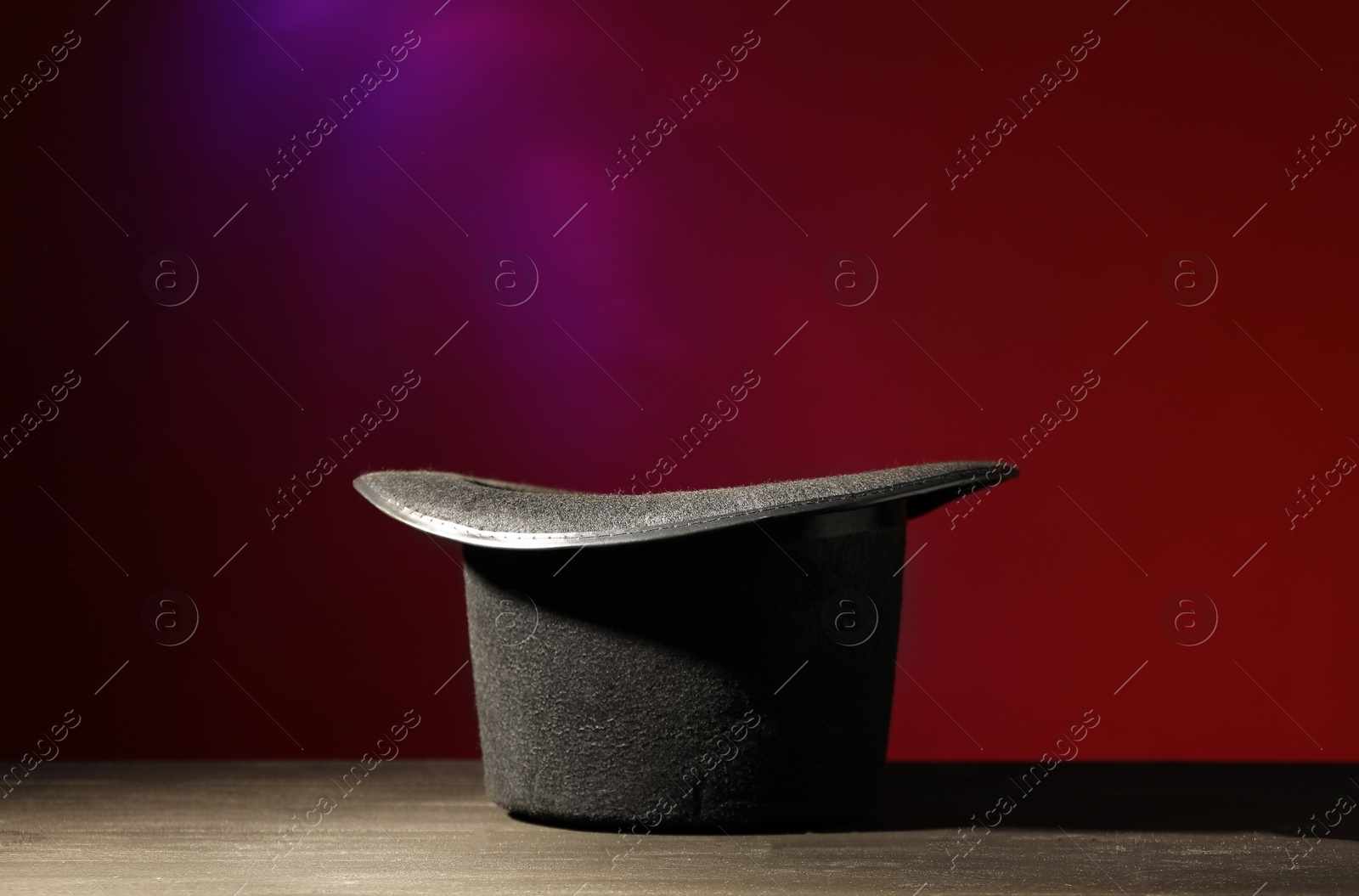 Photo of Magician's hat on black wooden table against color background