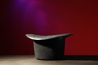 Photo of Magician's hat on black wooden table against color background