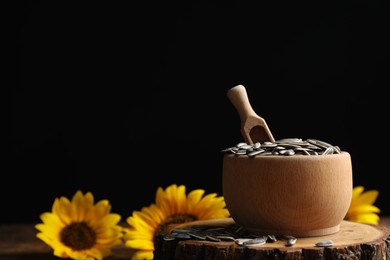 Photo of Raw sunflower seeds on wooden stand against black background. Space for text