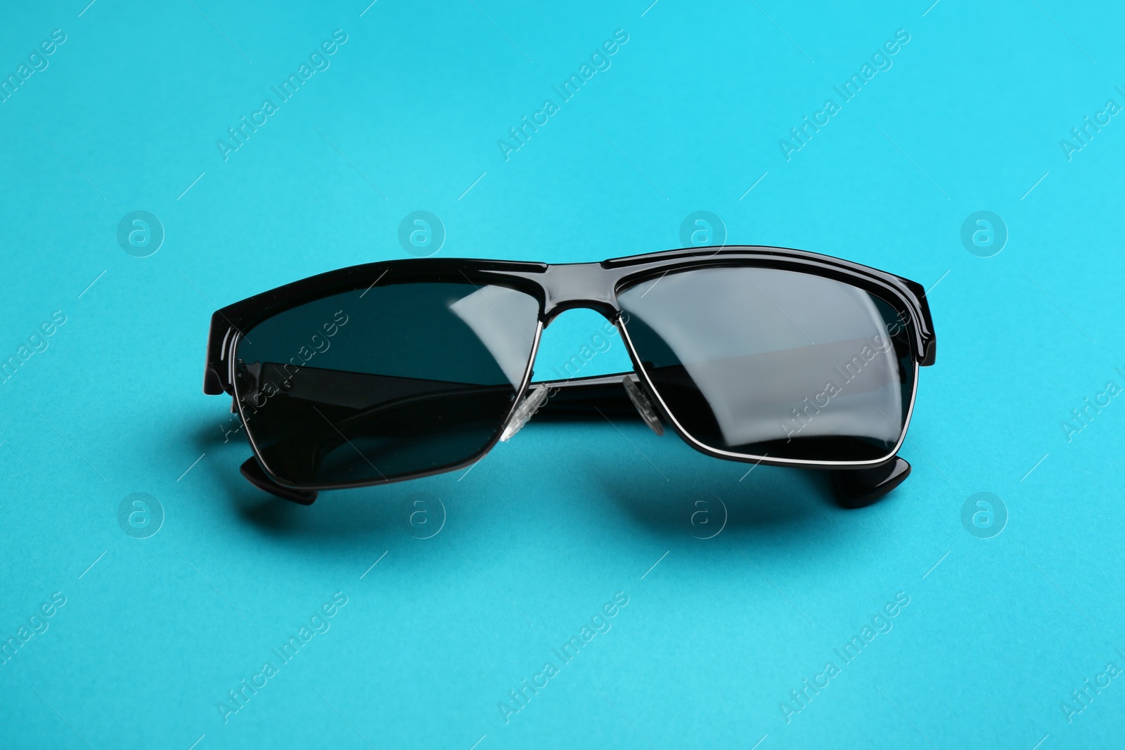 Photo of Stylish sunglasses on blue background. Fashionable accessory