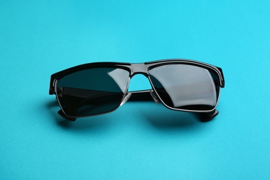 Photo of Stylish sunglasses on blue background. Fashionable accessory