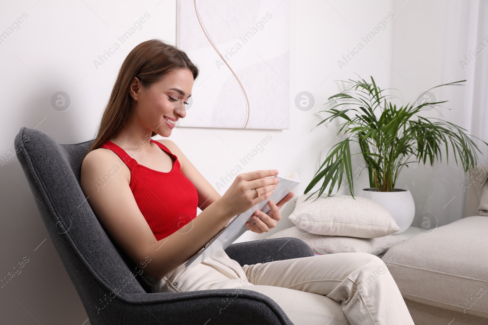 Photo of Young woman reading cooking magazine at home