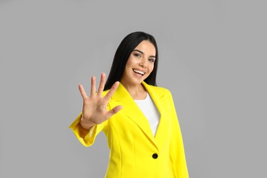 Photo of Woman showing number five with her hand on grey background