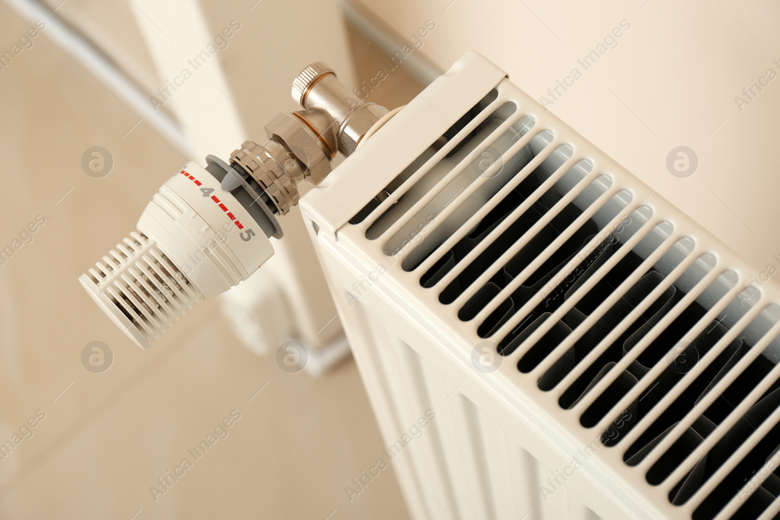 Photo of Heating radiator with thermostat near wall indoors, closeup