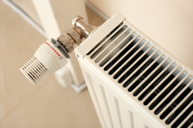 Photo of Heating radiator with thermostat near wall indoors, closeup