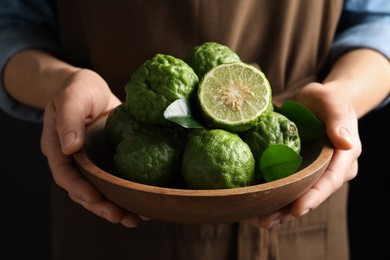 Photo of Woman holding wooden bowl with fresh ripe bergamot fruits on black background, closeup