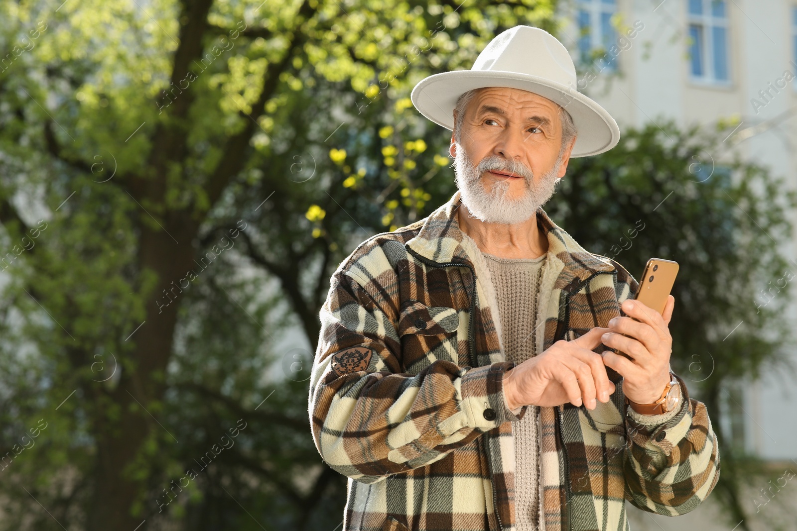 Photo of Handsome senior man using smartphone outdoors, space for text