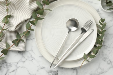 Stylish setting with cutlery, napkin, eucalyptus branches and plates on white marble table, flat lay