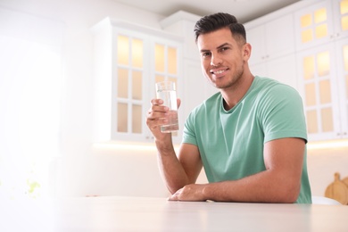 Man holding glass of pure water at table in kitchen. Space for text