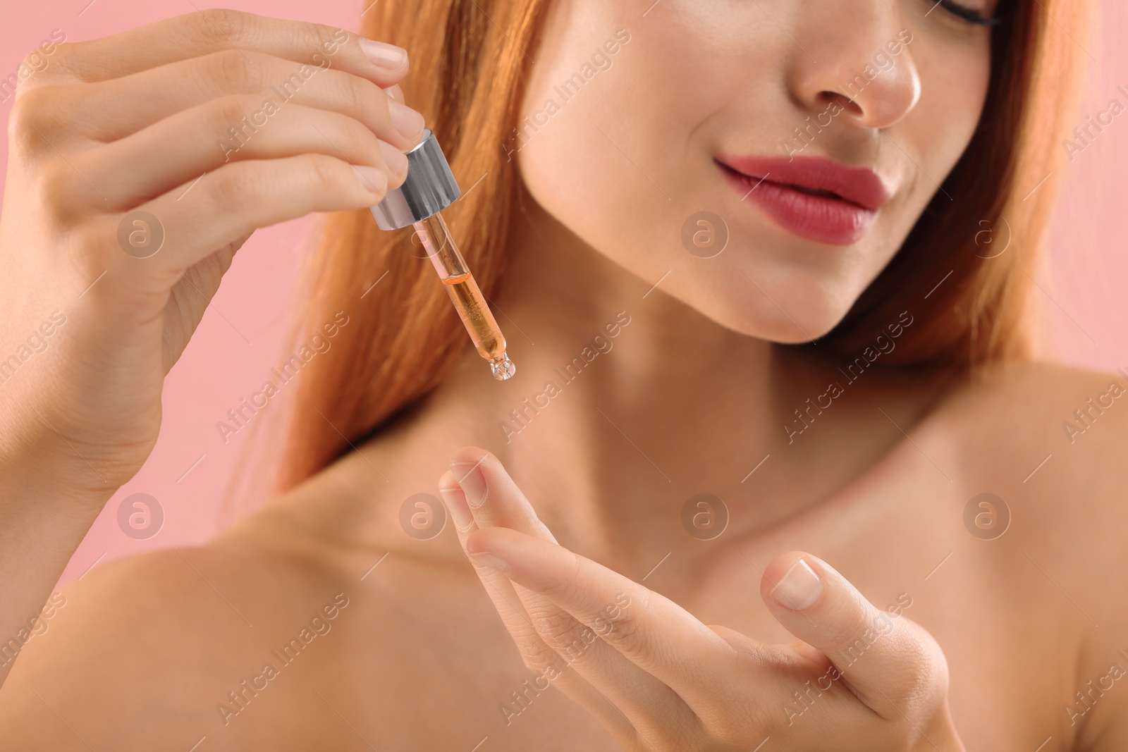 Photo of Beautiful young woman applying cosmetic serum onto her finger on pink background, closeup