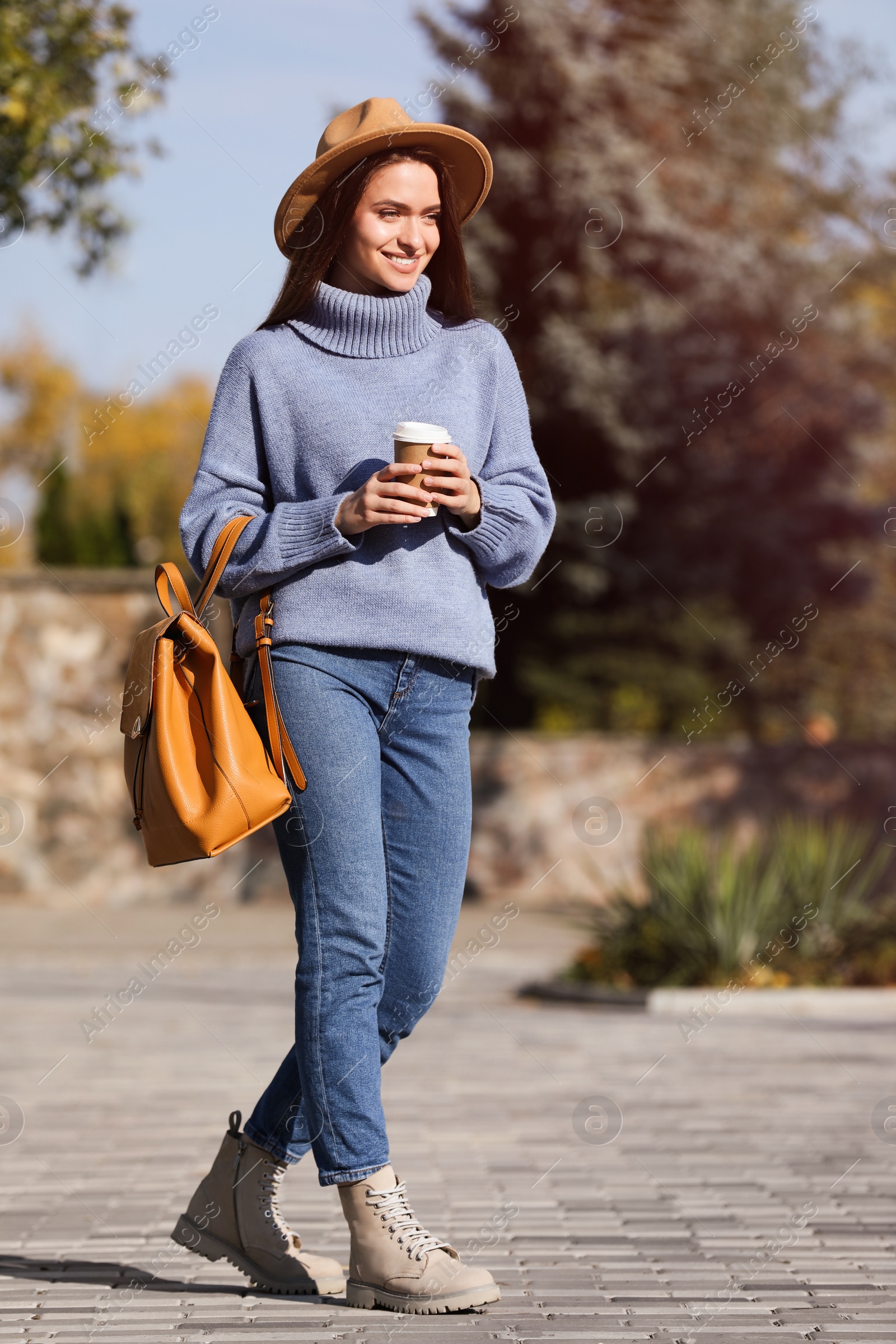 Photo of Young woman with stylish backpack and hot drink on autumn day