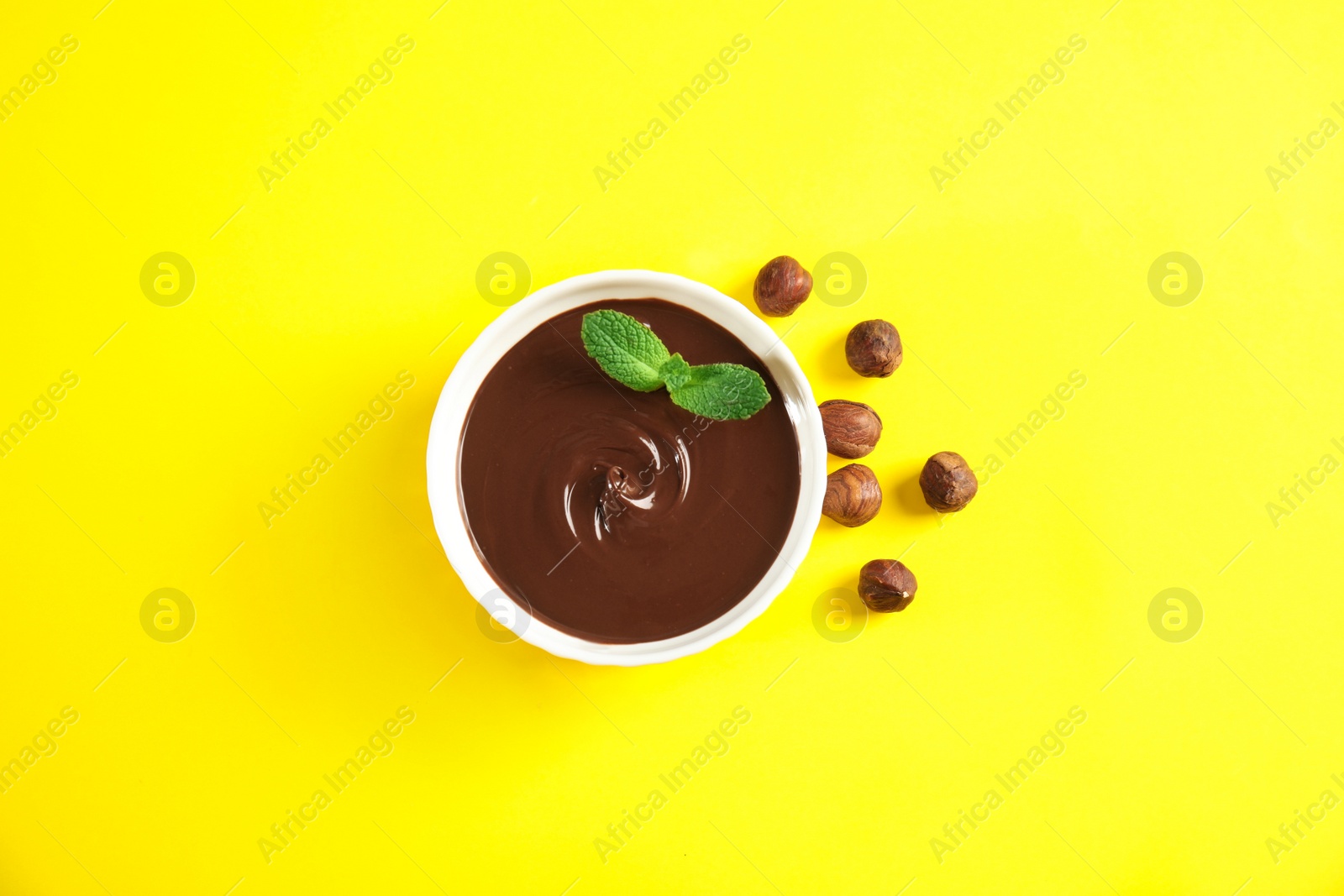 Photo of Ceramic bowl with sweet chocolate cream, hazelnuts and mint on color background, top view