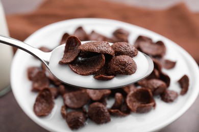 Photo of Breakfast cereal. Eating chocolate corn flakes and milk with spoon from bowl on table, closeup