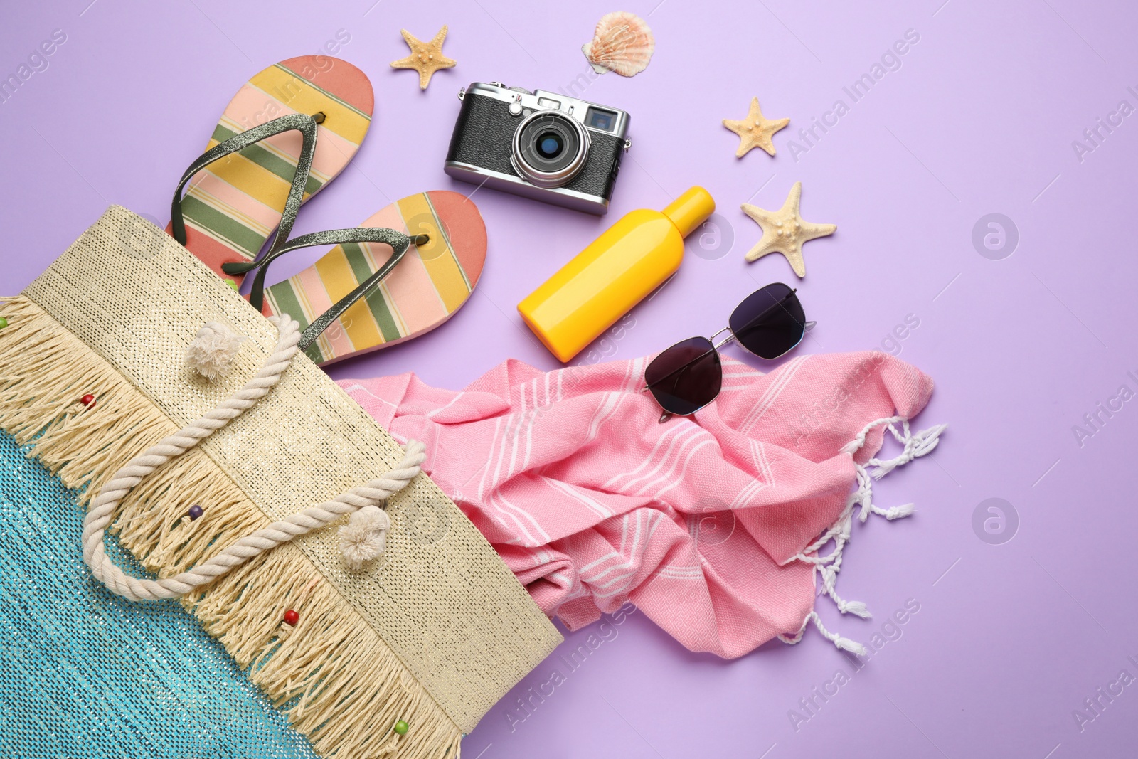 Photo of Stylish bag with beach accessories on violet background, flat lay