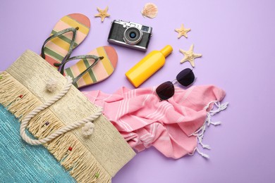 Stylish bag with beach accessories on violet background, flat lay