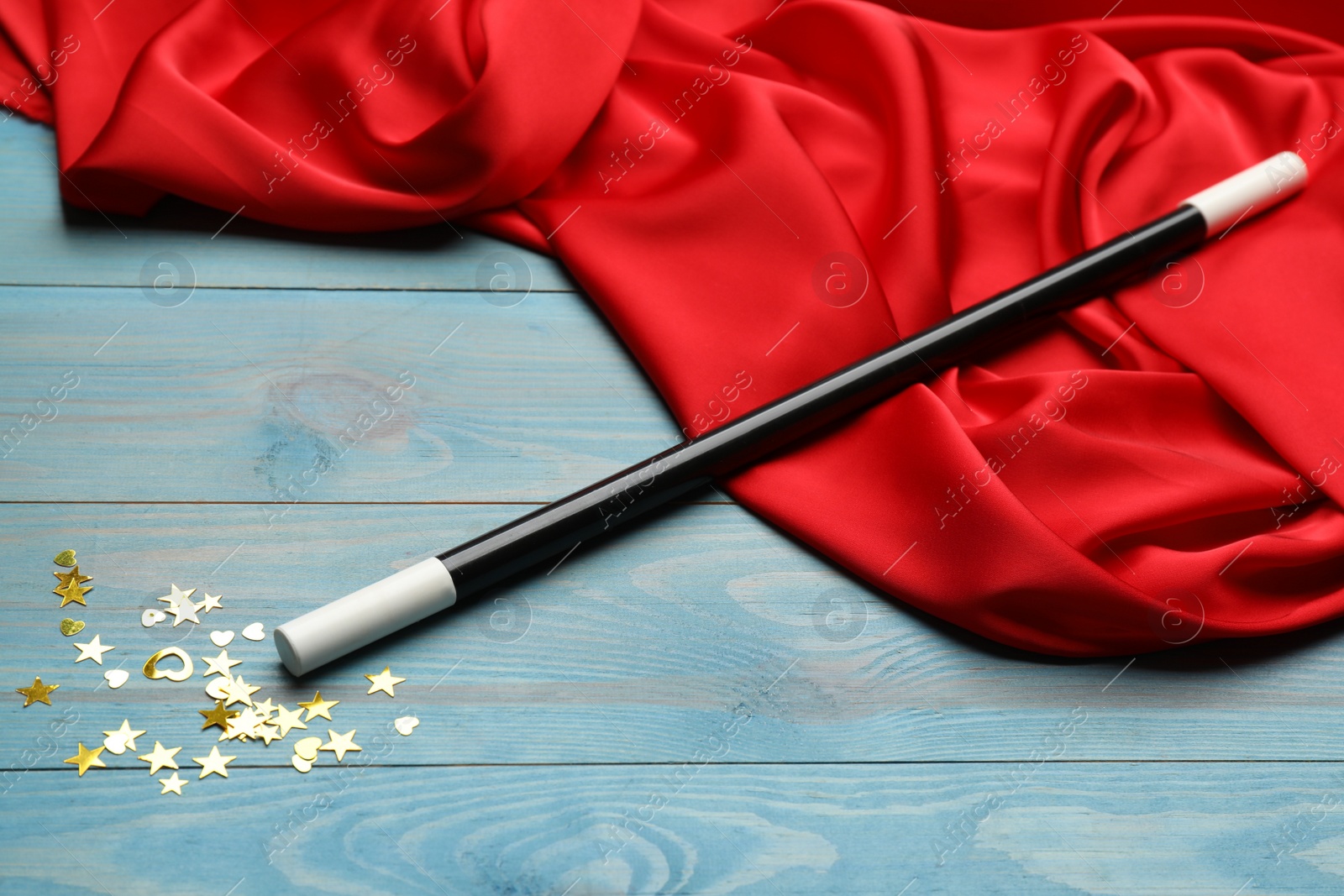 Photo of Beautiful black magic wand, confetti and red fabric on turquoise wooden table