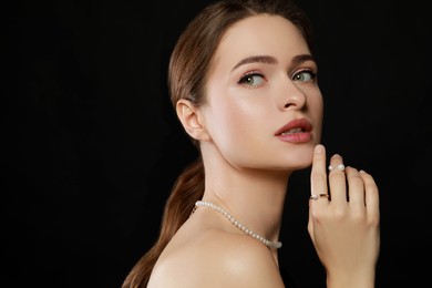 Young woman wearing elegant pearl jewelry on black background, space for text
