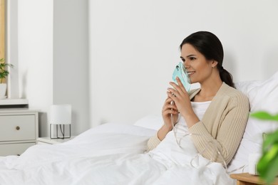 Young woman using nebulizer on bed at home, space for text
