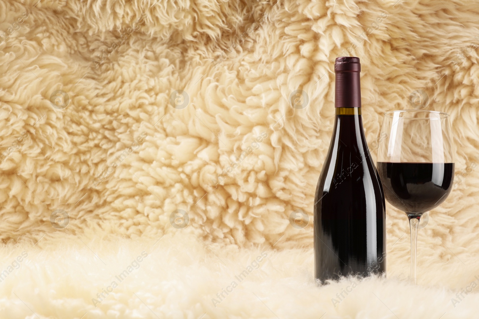 Photo of Stylish presentation of delicious red wine in bottle and glass on fluffy surface. Space for text