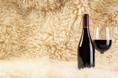 Stylish presentation of delicious red wine in bottle and glass on fluffy surface. Space for text