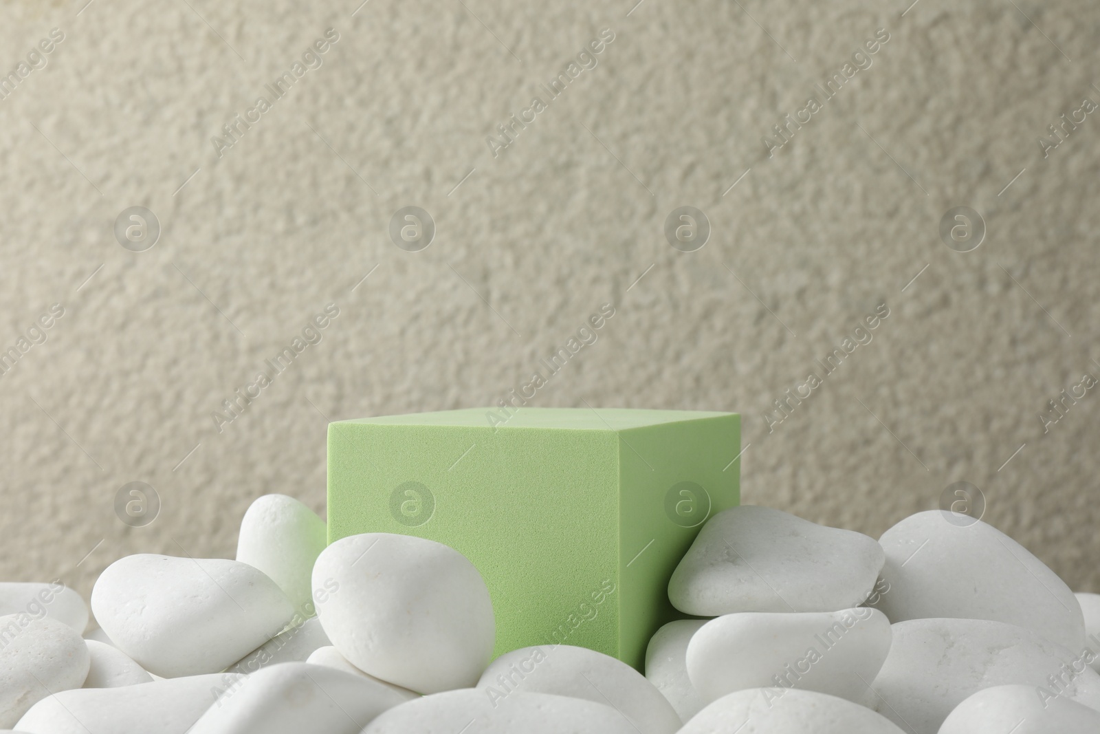 Photo of Presentation for product. Light green cube podium and white pebbles on blurred background. Space for text