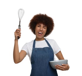 Emotional young woman in apron holding bowl and whisk on white background