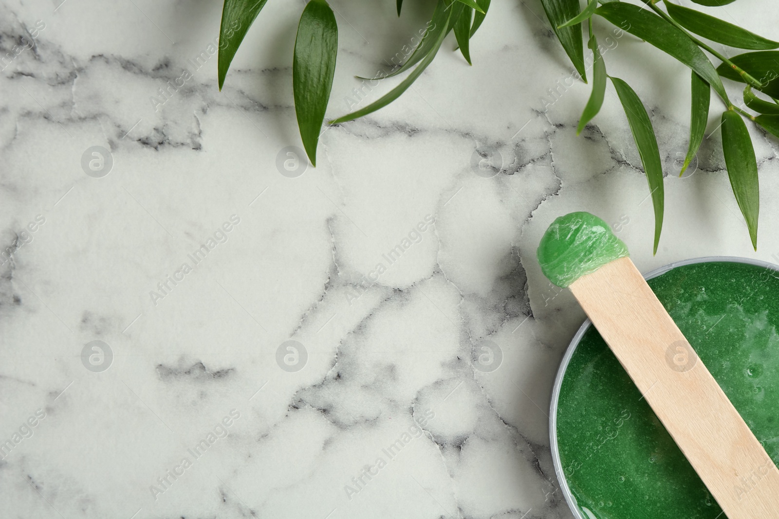 Photo of Spatula with wax and leaves on white marble table, flat lay. Space for text