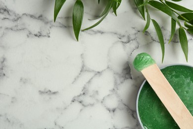 Photo of Spatula with wax and leaves on white marble table, flat lay. Space for text