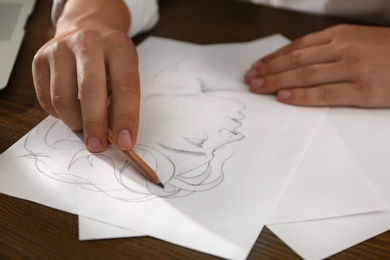Photo of Man drawing portrait with pencil on sheet of paper at wooden table, closeup