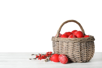 Photo of Wicker basket with painted red Easter eggs on table against white background, space for text