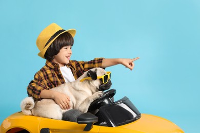 Photo of Little boy with his dog in toy car on light blue background
