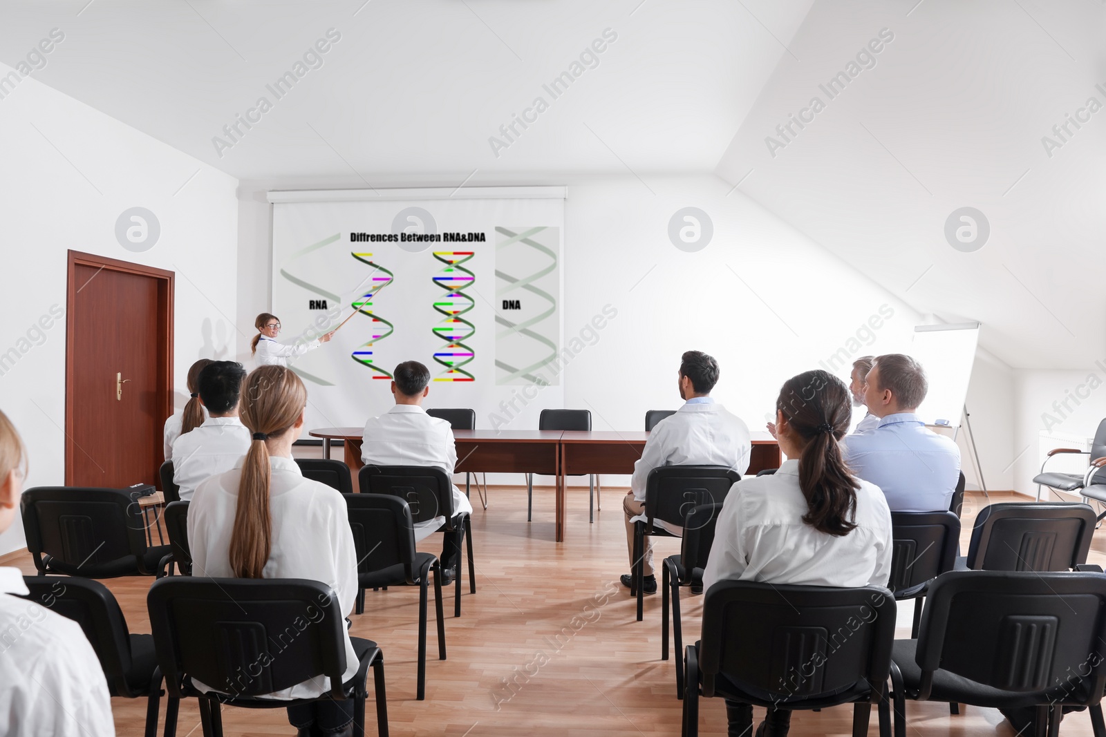 Image of Lecture about difference between RNA and DNA. Professor using projection screen with illustration to audience in conference room