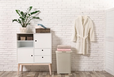 Photo of Furniture with clean towels and robe near brick wall in bathroom