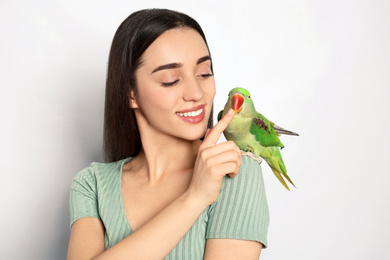 Young woman with Alexandrine parakeet on light background. Cute pet