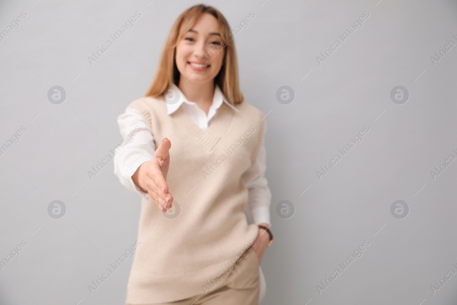 Photo of Happy young woman offering handshake on light grey background. Space for text