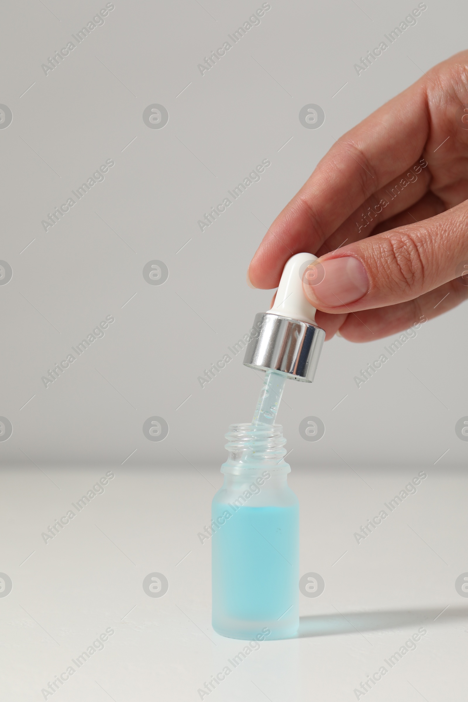 Photo of Woman with cosmetic serum at white table, closeup
